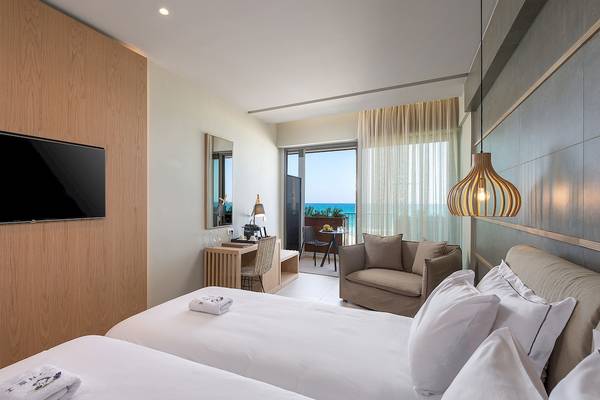 Innenansicht des Ikones Seafront Luxury Suites Hotels mit zwei Betten, Schreibtisch und Meerblick.