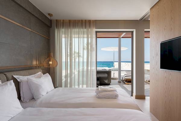 Zimmer im Ikones Seafront Luxury Suites mit Blick auf das Meer und Außenbereich mit Whirlpool und Sonnenschirm.