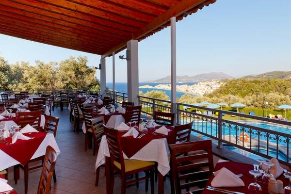Außenterrasse des Arion Hotel Samos mit Tischen und Stühlen, Ausblick auf das Meer und Berge.