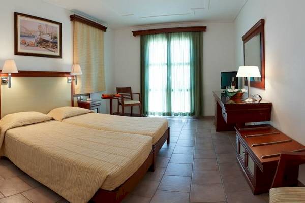 Innenansicht eines Doppelzimmers im Arion Hotel Samos mit zwei Betten, Nachttischen, einem Stuhl, einem Schreibtisch und einem Fernseher.