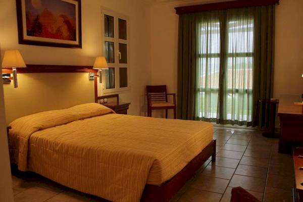 Innenansicht eines Schlafzimmers im Arion Hotel Samos mit Bett, Nachttischen und Fenstern.