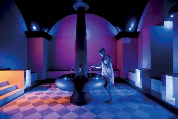 Eine Frau steht in der Elite Suites by Rhodes Bay Sauna und wäscht ihre Hände an einem Brunnen.