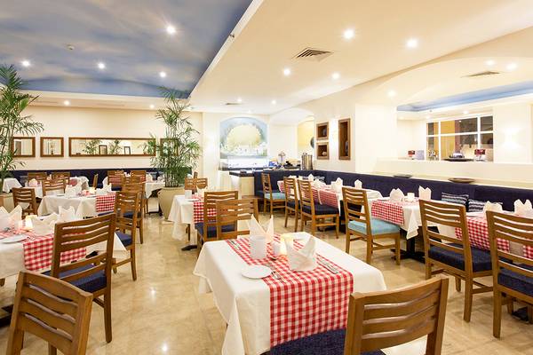 Innenansicht des Restaurants im Three Corners Ocean View Hotel mit roten und weißen Tischdecken und Holzstühlen.