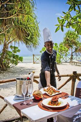 Ein Chefkoch serviert ein Essen am Tisch auf dem Strand.