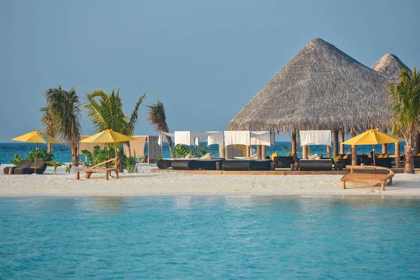 Strandszene des Drift Thelu Veliga Retreat mit Sonnenliegen, gelben Sonnenschirmen und einer großen runden Hütte