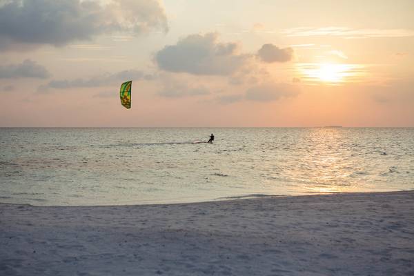 Sonnenuntergang am Strand mit einem Kitesurfer im Wasser.