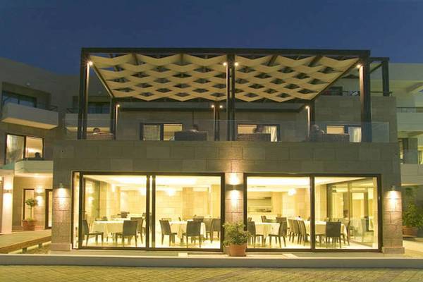 Außenansicht des D'Andrea Mare Beach Hotels bei Nacht mit hell beleuchteten Glasfassaden und Terrasse.