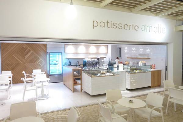 Innenansicht der Patisserie Amelie mit modernem Design, weißen Möbeln und einer Person hinter dem Tresen.
