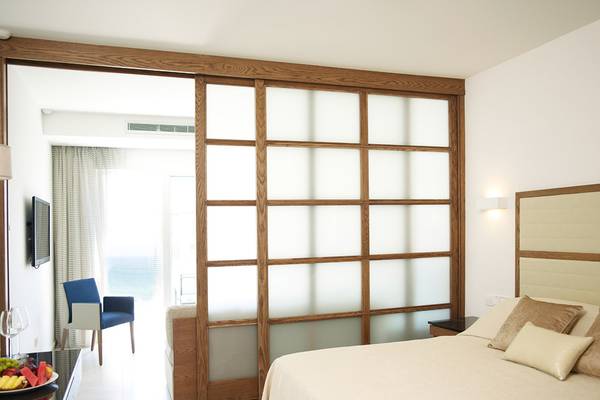 Innenansicht eines Zimmers im Sunrise Pearl Hotel mit einem Bett, einem Tisch mit Früchten, einem Fernseher und einer Tür zum Balkon.