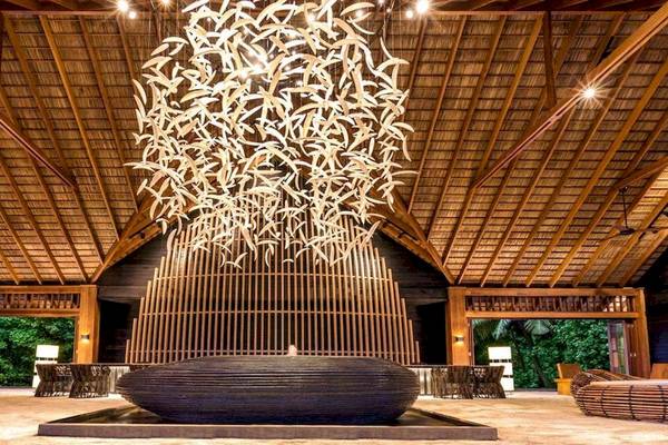 Lobby des Hurawalhi Island Resorts mit einer großen dekorativen Deckenlampe und Sitzgelegenheiten.