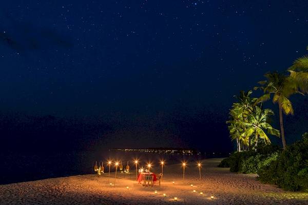 Romantisches Essen auf dem Strand des Hurawalhi Island Resorts bei Nacht mit vielen Kerzen und Sternenhimmel.
