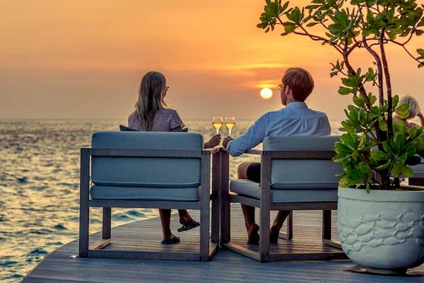Paar auf Balkon genießt den Sonnenuntergang im Hurawalhi Island Resort