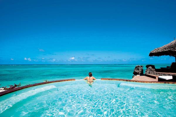 Ein Schwimmbecken am Rand des Meeres mit einer Frau im Wasser im Karafuu Beach Resort & Spa.