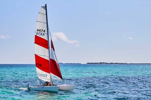 Ein Segelboot mit rot-weißem Segel fährt im blauen Meer in der Nähe von Hurawalhi Island Resort.