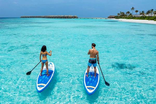 Zwei Personen stehen auf Stand-Up-Paddleboards im kristallklaren Wasser vor dem Hurawalhi Island Resort.