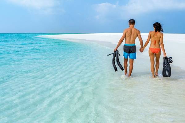 Paar am Strand von Hurawalhi Island Resort mit Schnorchelausrüstung in der Hand.