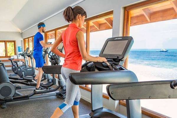 Fitnessstudio im Hurawalhi Island Resort mit zwei Personen auf Laufbändern und Blick auf das Meer.