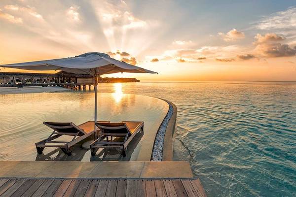 Sonnenuntergang am Pool des Hurawalhi Island Resort mit zwei Liegen und einem Sonnenschirm.