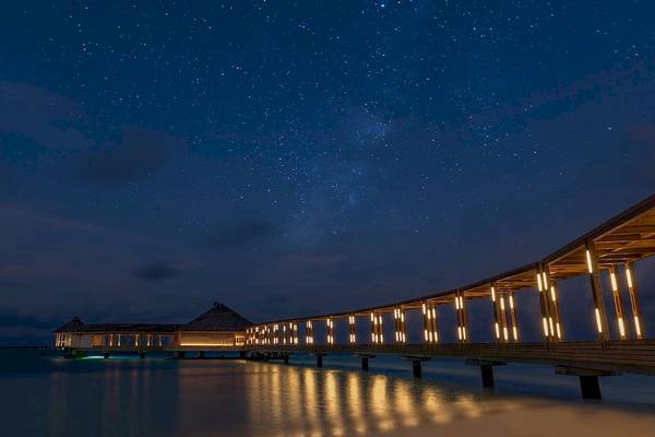 Nachtansicht des Hurawalhi Island Resorts mit Sternenhimmel und beleuchtetem Steg