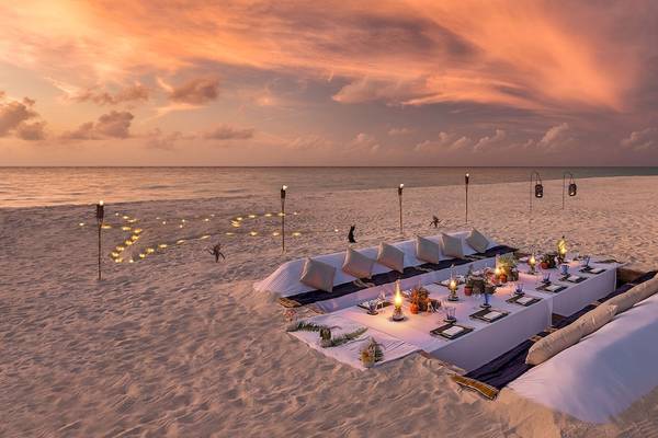 Ein romantisches Dinner-Setup auf dem Strand des Hurawalhi Island Resorts bei Sonnenuntergang.