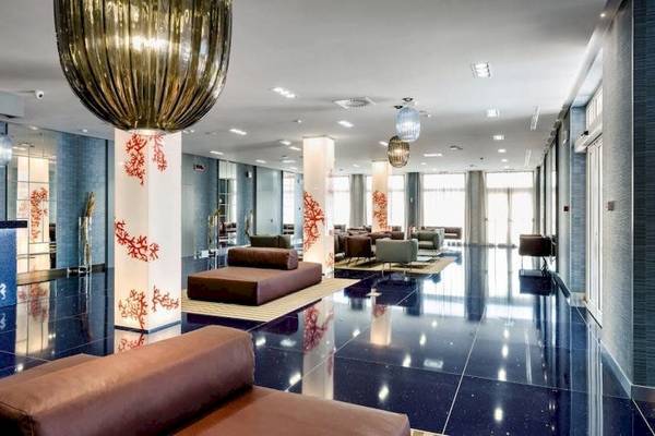 Lobby des Cala Ponte Hotels mit modernen Möbeln und einer großen Kronleuchter