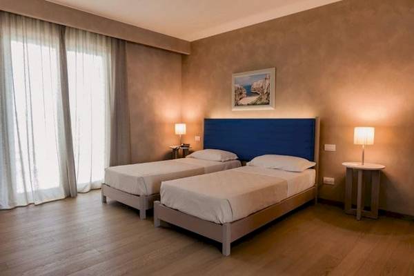Doppelzimmer im Cala Ponte Hotel mit zwei Betten, Nachttischen und Lampen.