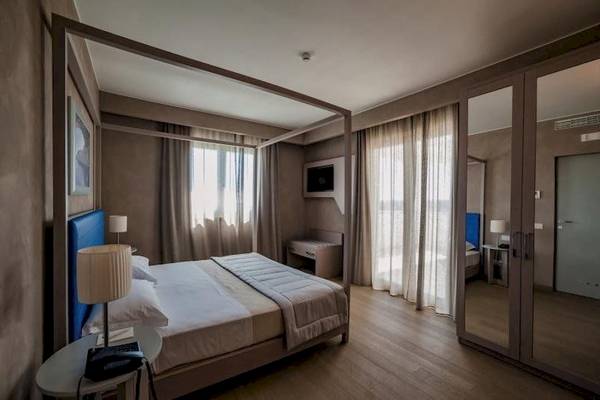 Ein elegantes Hotelzimmer im Cala Ponte Hotel mit einem großen Bett, zwei Nachttischen und Spiegeln.