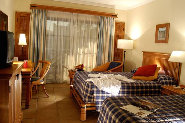 Zwei Doppelbetten in einem Hotelzimmer von Sharm Plaza, mit Kleidern und Zeitschriften auf den Betten, einem Schreibtisch und Stühlen.