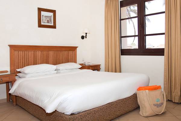 Ein Bett im Hotelzimmer des Sharm Plaza Hotels mit weißen Laken und Kissen, neben einem Tisch mit Telefon.