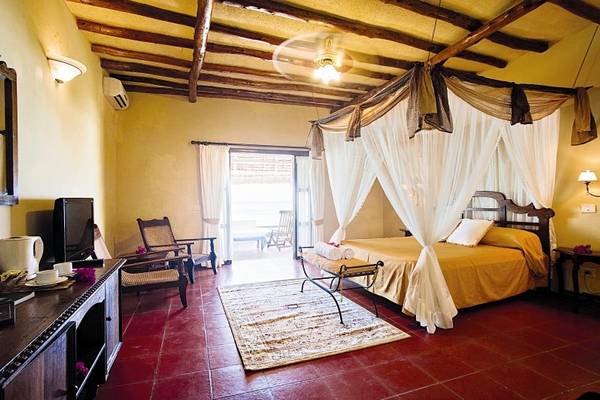 Schlafzimmer im Karafuu Beach Resort & Spa mit einem Bett, Deckenventilator, Fernseher und einem Tisch.