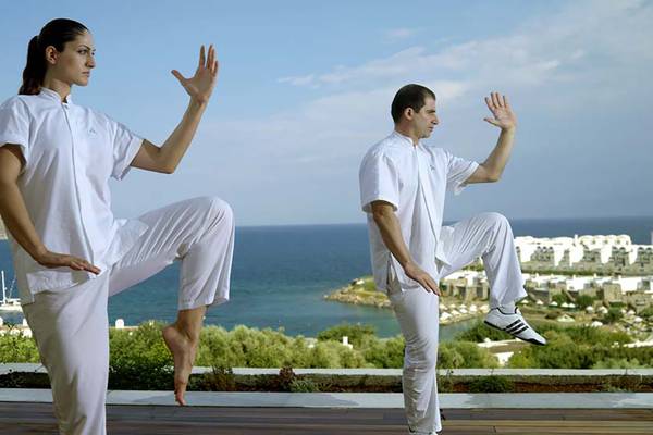 Zwei Personen praktizieren Yoga auf der Terrasse des Porto Elounda Golf & Spa Resorts am Strand.