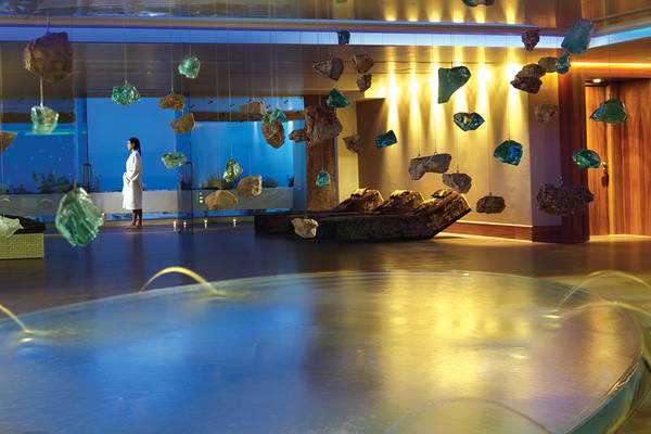 Innenpool im Porto Elounda Golf & Spa Resort mit hängenden Kristallen und einer Frau im weißen Bademantel.