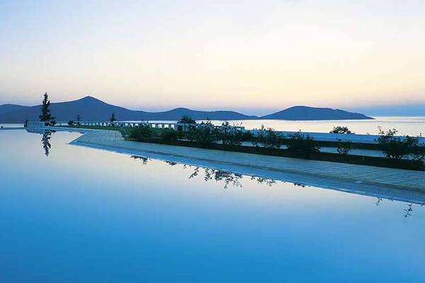 Pool des Porto Elounda Golf & Spa Resorts bei Sonnenuntergang mit Blick auf die Berge und das Meer.