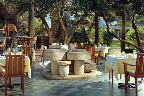 Restaurant im Freien im Porto Elounda Golf & Spa Resort mit Tischen, Stühlen und einem Brunnen.