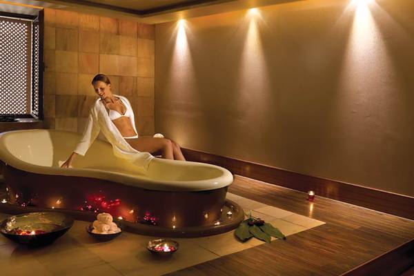 Eine Frau im weißen Bademantel sitzt in einer Badewanne im Spa des Porto Elounda Golf & Spa Resorts.