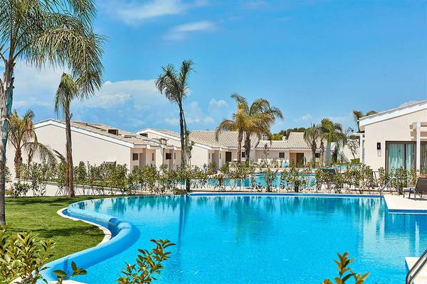 Außenpool des Atlantica Mare Ayia Napa mit umgebenden Gebäuden und Palmen.