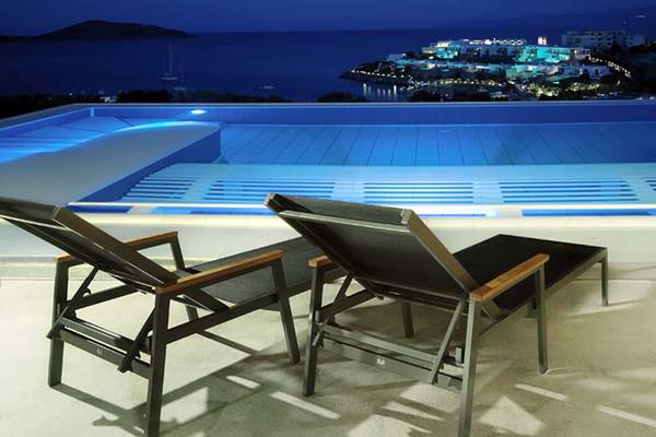 Nachtansicht des Außenpools des Porto Elounda Golf & Spa Resorts mit Blick auf das Meer und die Stadt.