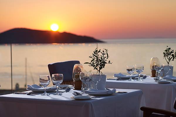 Außentisch im Porto Elounda Golf & Spa Resort bei Sonnenuntergang mit Blick auf das Meer und die Berge.