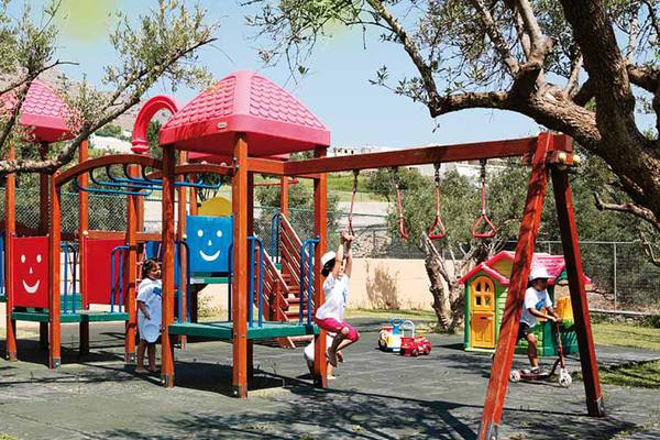 Kinderspielplatz im Freien im Porto Elounda Golf & Spa Resort mit bunten Spielgeräten und Bäumen.