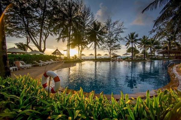 Der Pool des Katathani Phuket Beach Resorts bei Sonnenuntergang mit Liegestühlen und Sonnenschirmen.