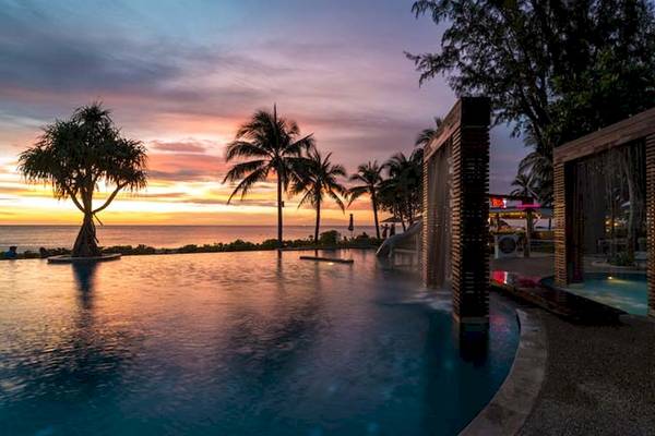 Katathani Phuket Beach Resort Pool bei Sonnenuntergang mit Blick auf den Ozean und Palmen.