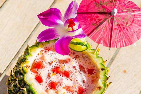 Cocktail in einer Ananasschale mit einem roten Schirm und einer Blume