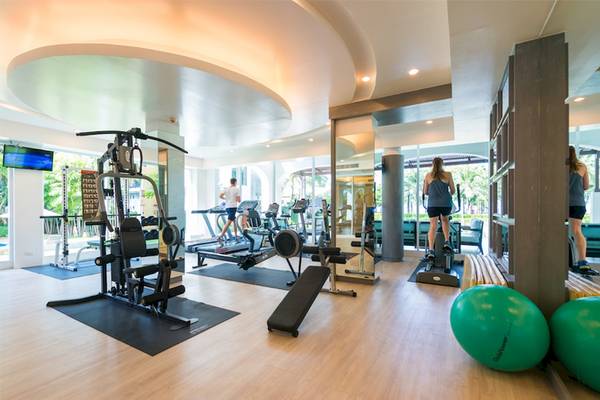 Fitnessstudio im Katathani Phuket Beach Resort mit Laufbändern, Gewichtsmaschinen und einer Frau, die auf einem Rudergerät trainiert.