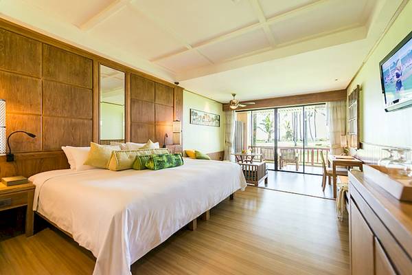 Innenansicht eines Schlafzimmers im Katathani Phuket Beach Resort mit großem Bett, Holzmöbeln und Balkonzugang.
