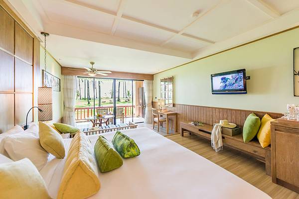 Innenansicht einer Suite im Katathani Phuket Beach Resort mit einem großen Bett, grünen Kissen und einem Fernseher an der Wand.