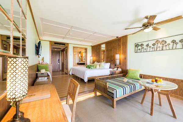 Innenansicht eines Zimmers im Katathani Phuket Beach Resort mit Bett, Esstisch und Wohnzimmerbereich.