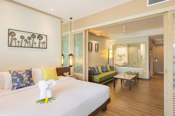 Innenansicht eines Hotelzimmers im Katathani Phuket Beach Resort mit Bett, Sofa und Badewanne.