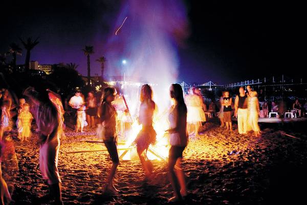Menschen feiern um ein großes Feuer auf dem Strand des Terrace Beach Resorts bei Nacht.