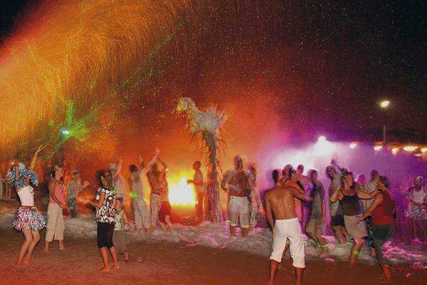 Gruppe von Menschen tanzt am Strand unter einem Feuerwerk und bunten Lichtern