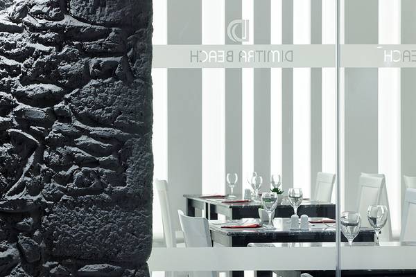 Innenansicht des Restaurants im Dimitra Beach Hotel & Suites mit schwarzen und weißen Tischplatten und weißen Stühlen.